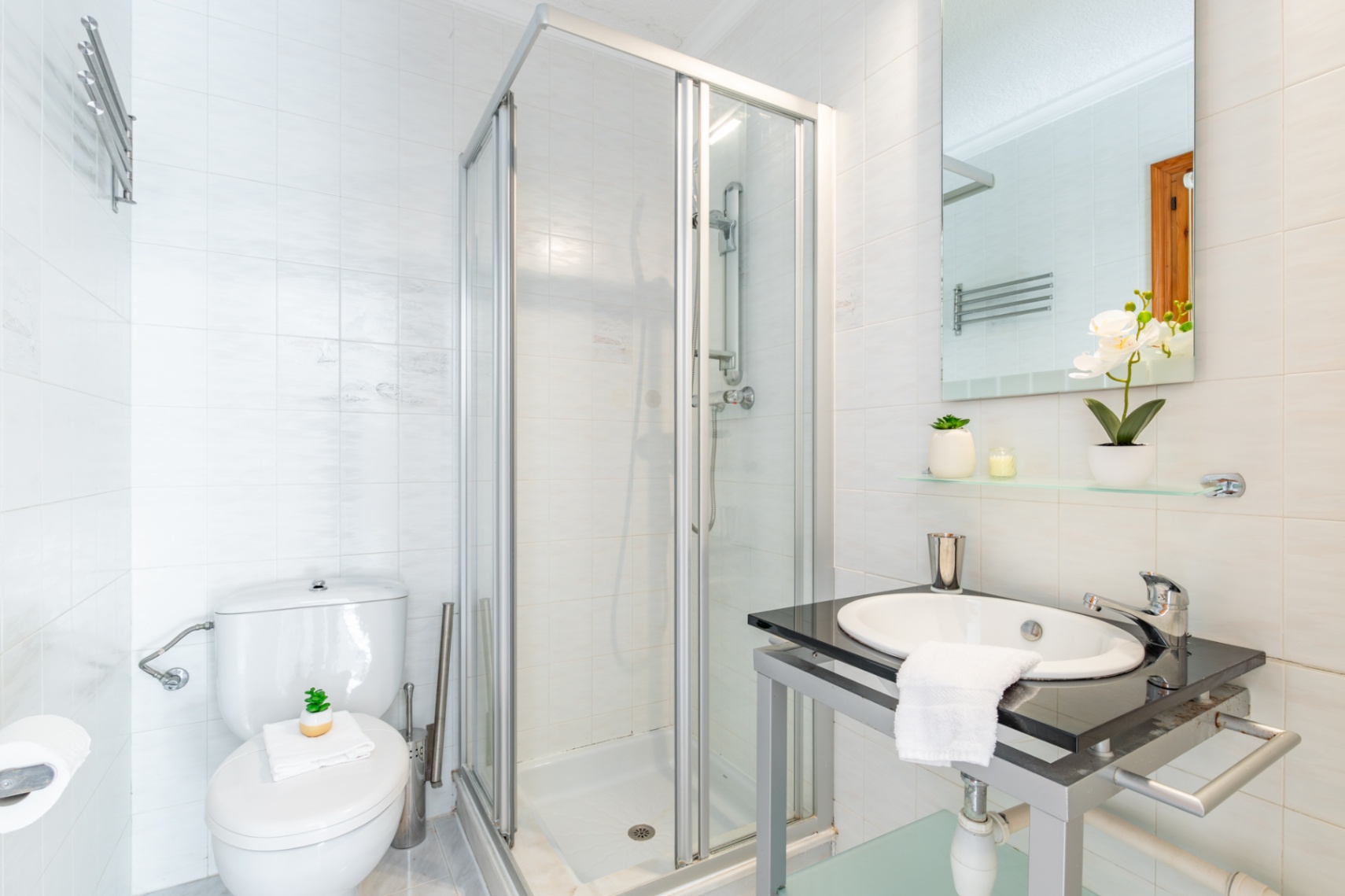 Salle de bain équipée de murs carrelés blancs, d'une cabine de douche vitrée et d'un lavabo encastré dans un plan de travail en pierre sombre.