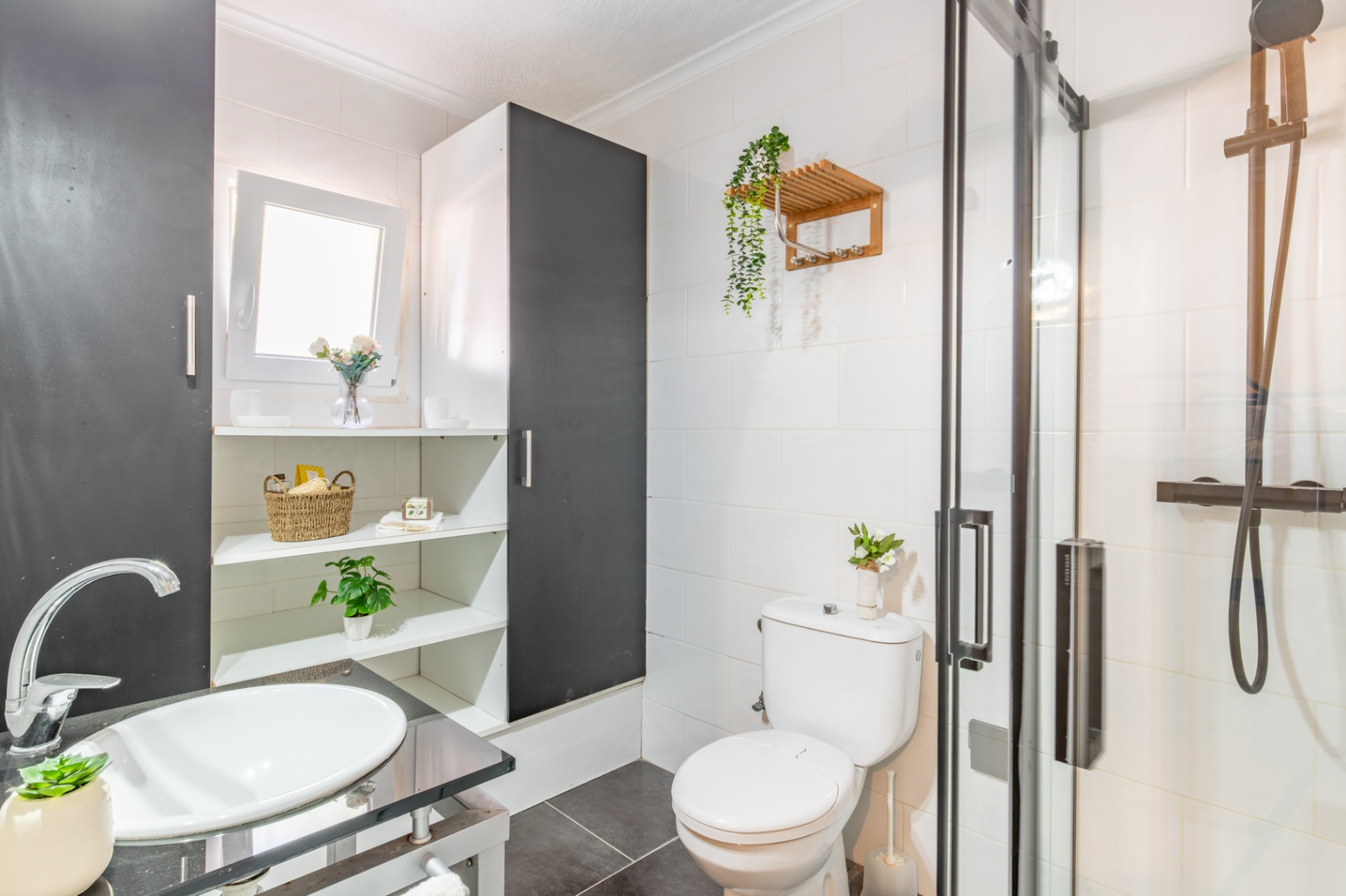 Salle de bain fonctionnelle avec douche à l'italienne, robinetterie noire et vasque blanche. Elle dispose d'étagères intégrées et de carrelage mural blanc.