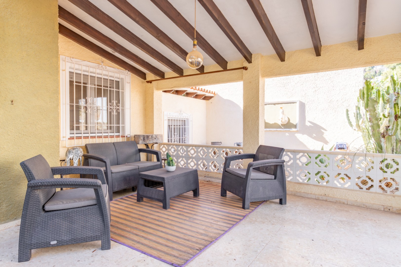 Terrasse couverte avec poutres en bois apparentes, mobilier de jardin en résine tressée grise et balustrade décorative traditionnelle.