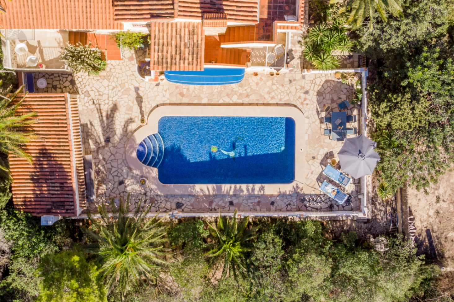 Vue aérienne de la vaste terrasse en pierre naturelle avec sa piscine de 42 m², son espace dînatoire et son solarium entouré de palmiers.