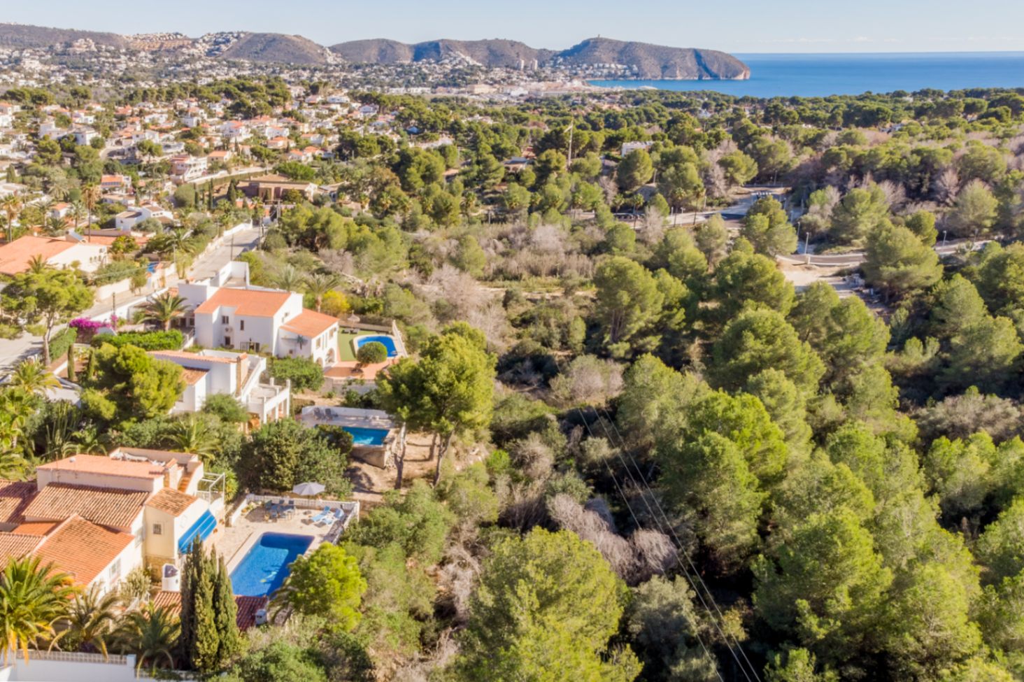 Vue aérienne soulignant l'emplacement privilégié bordant une zone verte protégée, avec vue panoramique sur la mer Méditerranée et la côte de Moraira.