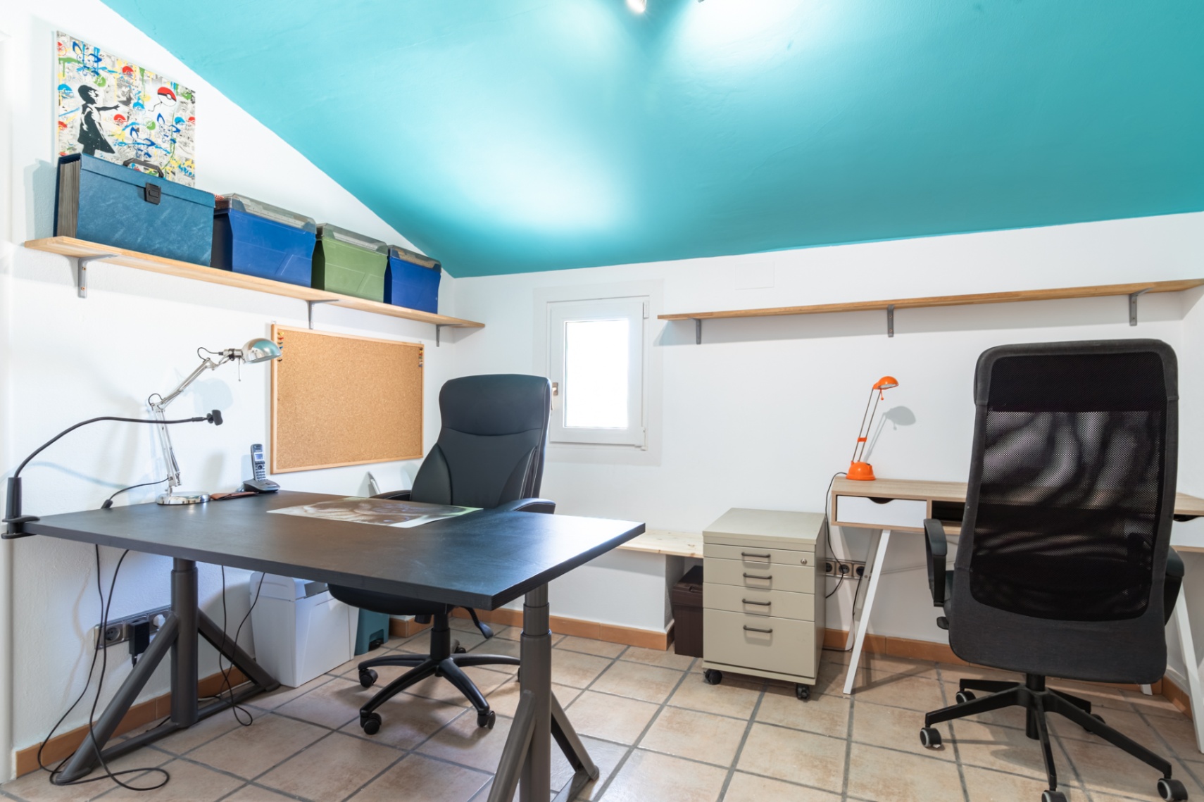 Bureau fonctionnel avec un plafond incliné turquoise, deux postes de travail, un sol en céramique et des étagères de rangement murales.