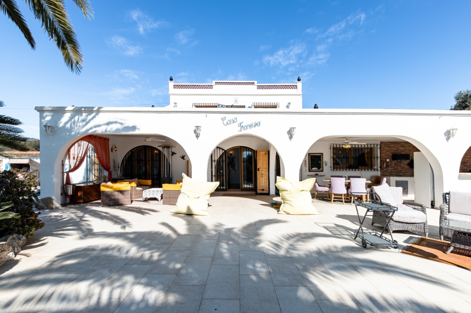 Façade blanche de style méditerranéen avec naya à arches, terrasse pavée et coins salon extérieurs sous l'enseigne "Casa Franziska".