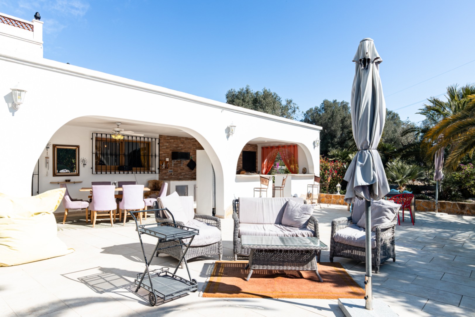 Grande terrasse extérieure avec salon de jardin en rotin et naya voûtée comprenant un espace dînatoire et une cuisine d'été équipée.