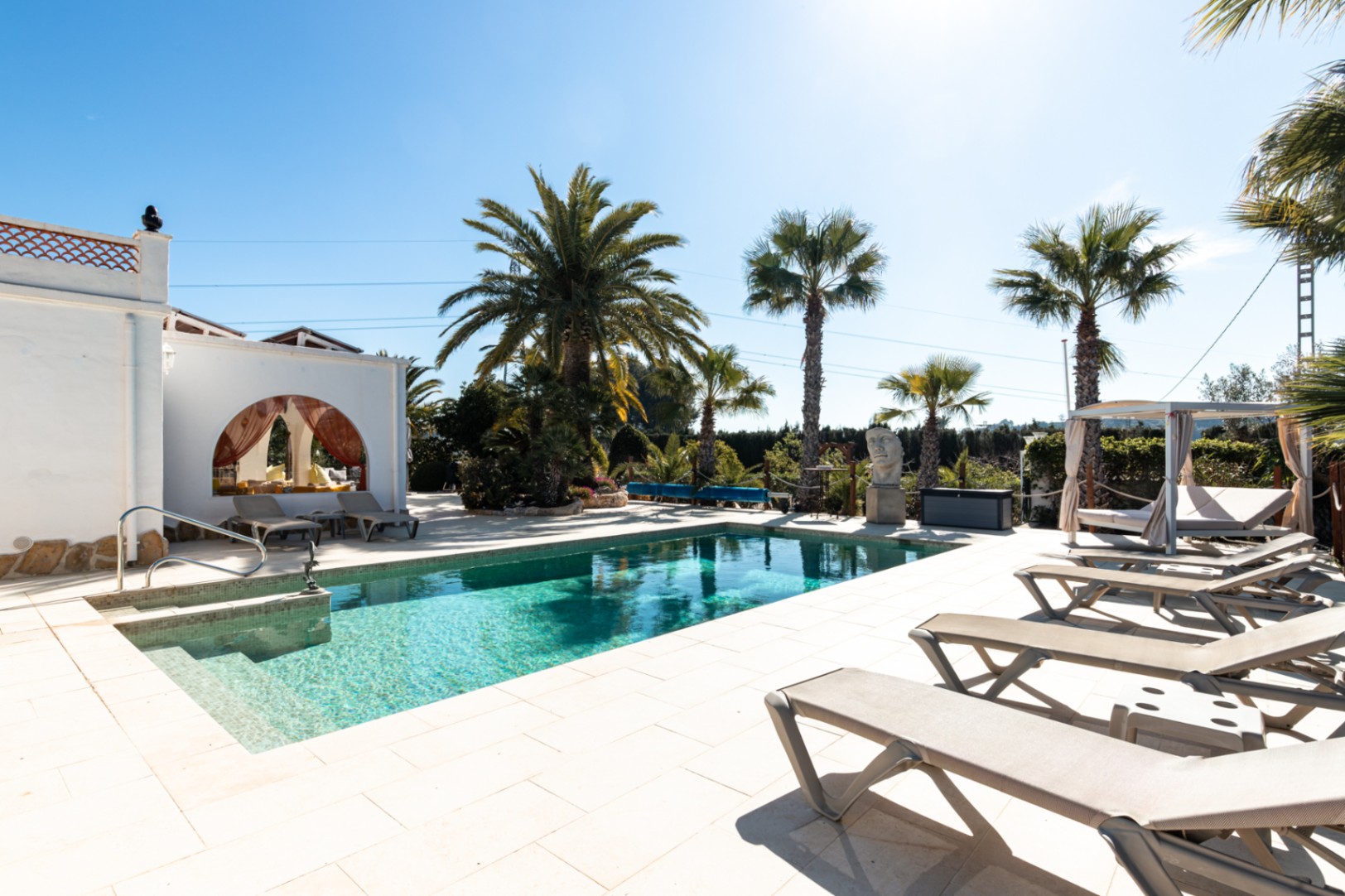 Piscine de 9,5x5m avec terrasse en pierre claire, espace de bronzage avec transats, cabane privée et jardin méditerranéen arboré.