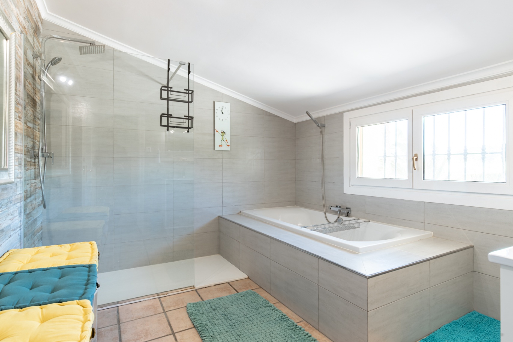 Salle de bain moderne avec douche à l'italienne, paroi vitrée et baignoire encastrée. Les murs sont revêtus de carreaux gris et le sol de dalles en terre cuite.