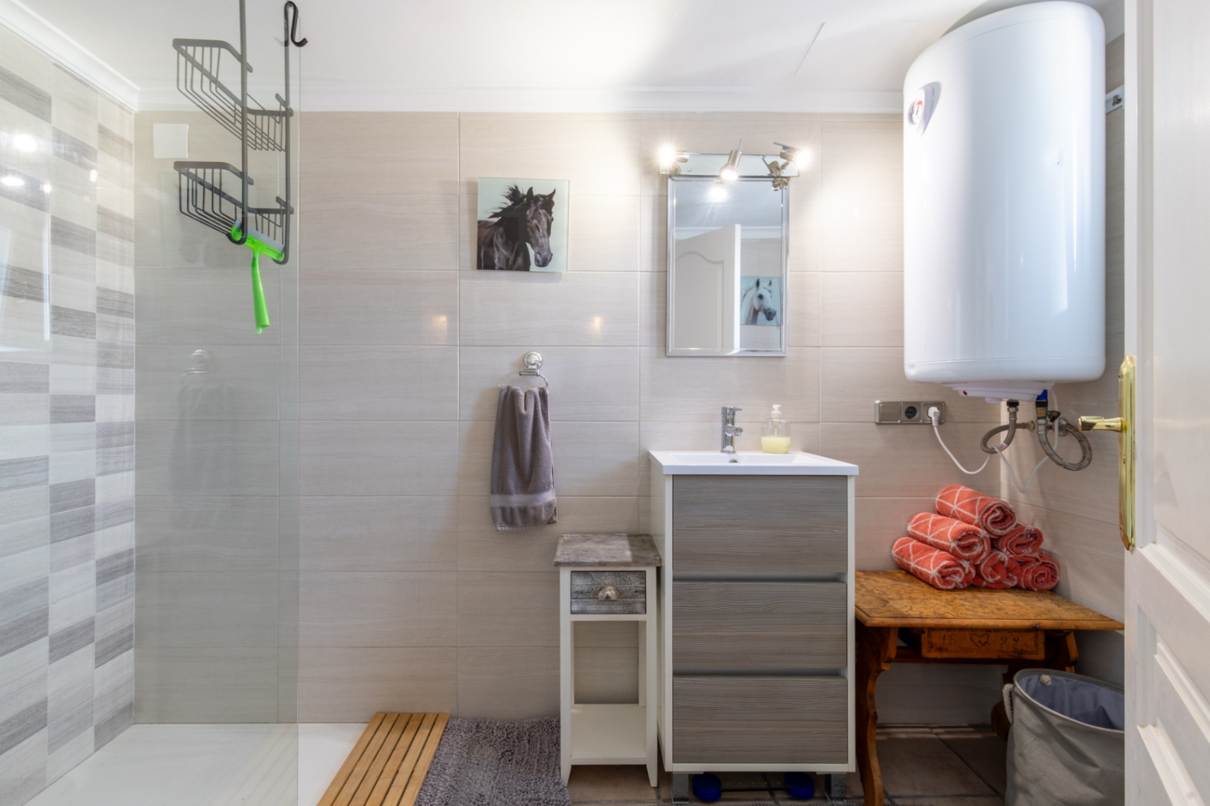 Salle de bains fonctionnelle avec douche à l'italienne, paroi vitrée et carrelage texturé. Elle comprend un meuble vasque gris, un chauffe-eau et des accents en bois.