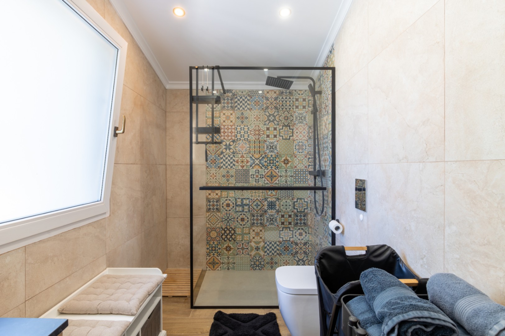 Salle de bains moderne avec douche à l'italienne, paroi à cadre noir et mur décoratif en carreaux de ciment, complétée par un sol imitation bois.