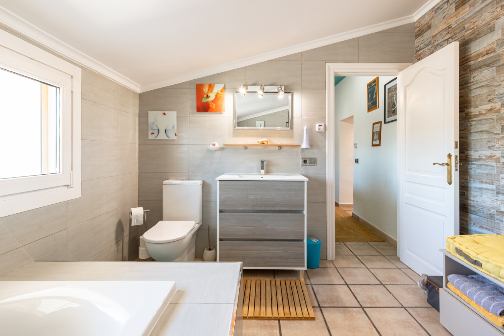 Salle de bains rénovée avec plafond incliné, meuble vasque en bois et carrelage mural grand format complété par un mur d'accent texturé.