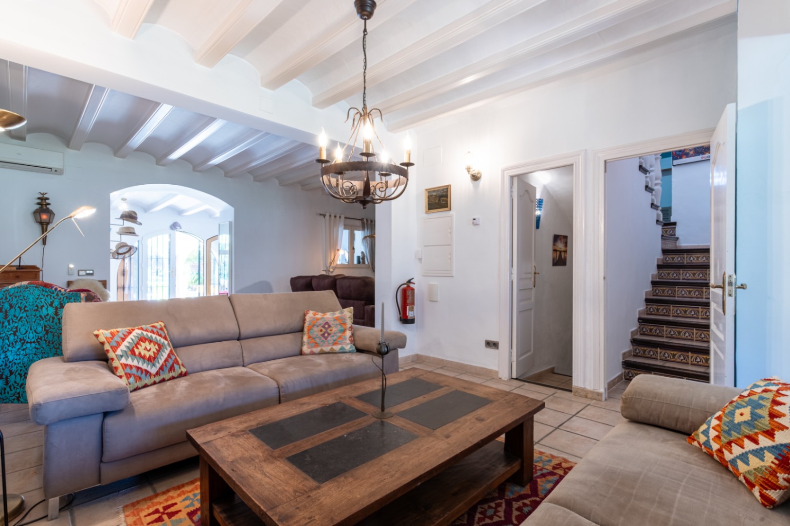 Salon avec plafonds à poutres blanches, sol en terre cuite et escalier orné d'azulejos. Une table basse en bois massif complète cet espace de vie chaleureux.