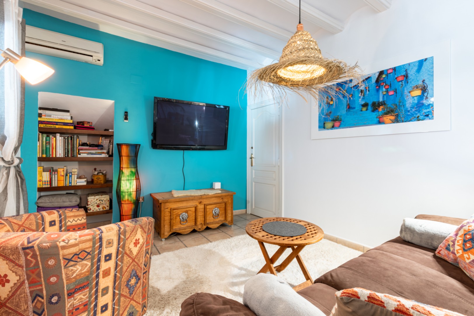 Salon chaleureux avec mur d'accent turquoise, poutres blanches et étagères encastrées. Comprend la climatisation, un mobilier rustique et une suspension artisanale en fibres naturelles.