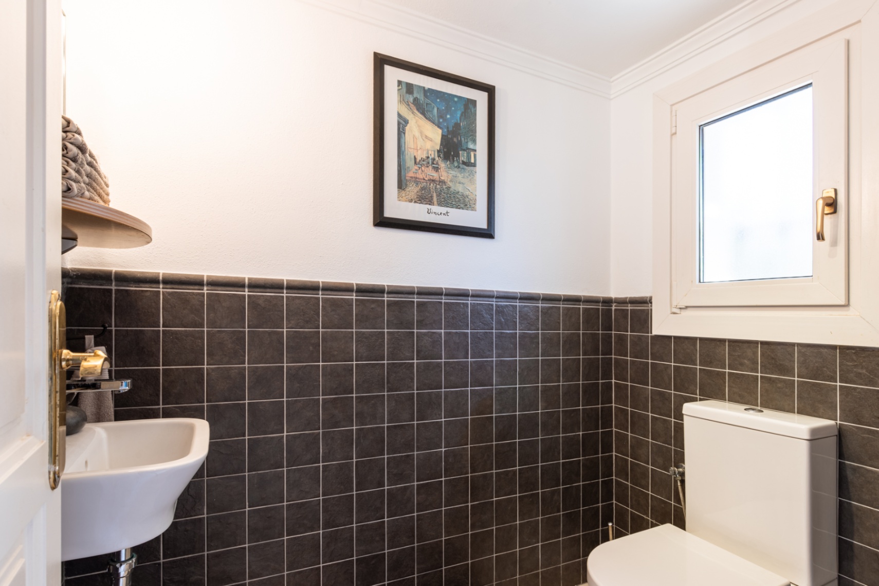 Toilettes invités fonctionnelles avec carrelage mural sombre texturé, lave-mains compact et fenêtre pour une ventilation naturelle.
