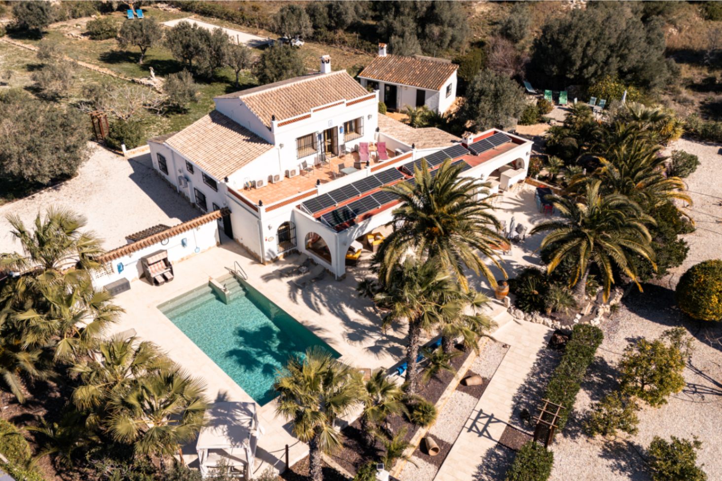Vue aérienne de la finca présentant la piscine, les terrasses en pierre et l'installation solaire sur la naya, le tout entouré d'un jardin méditerranéen.