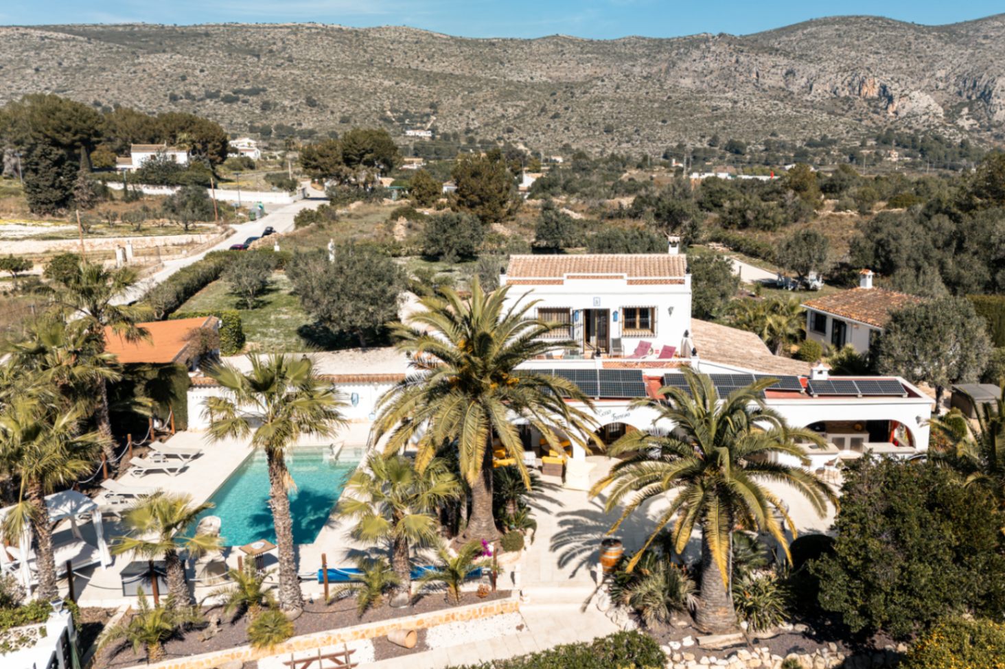 Vue aérienne de la propriété montrant la piscine, les panneaux solaires en toiture et le jardin paysager avec vue sur les montagnes.