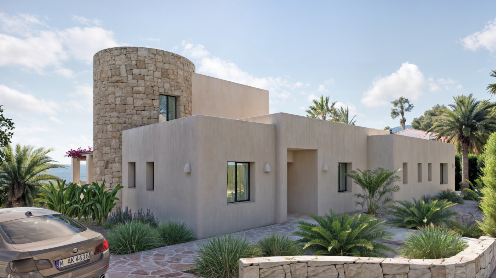 Façade de style Ibiza avec tour cylindrique en pierre naturelle, menuiseries en aluminium noir et jardin méditerranéen aux finitions épurées.