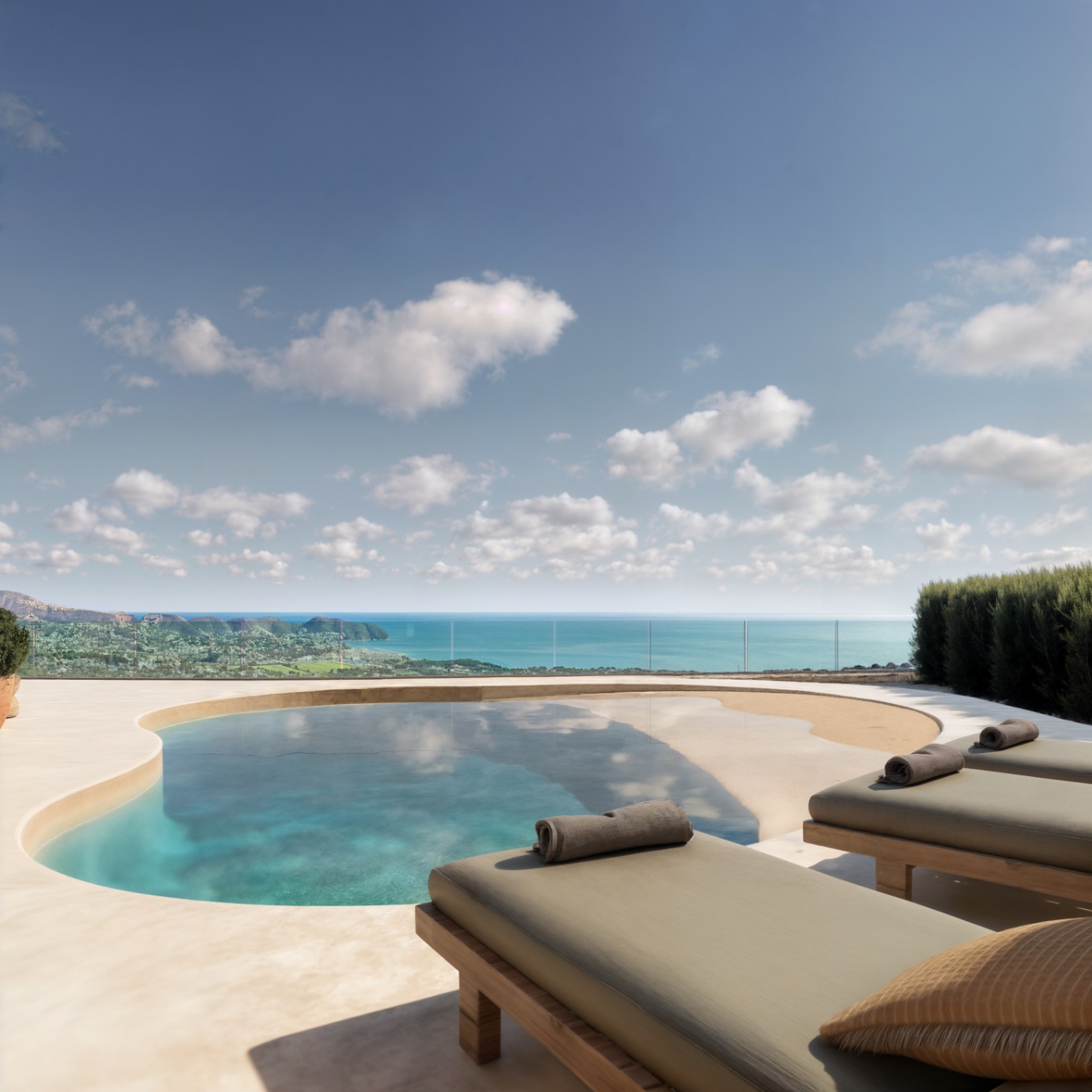 Terrasse extérieure avec piscine aux formes organiques, chaises longues en bois et vue panoramique sur la mer Méditerranée derrière un garde-corps en verre.