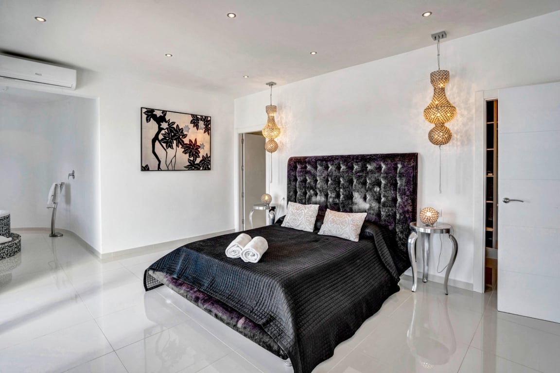 Chambre avec tête de lit en velours capitonné, sol en grès cérame poli, luminaires suspendus décoratifs et climatisation individuelle.