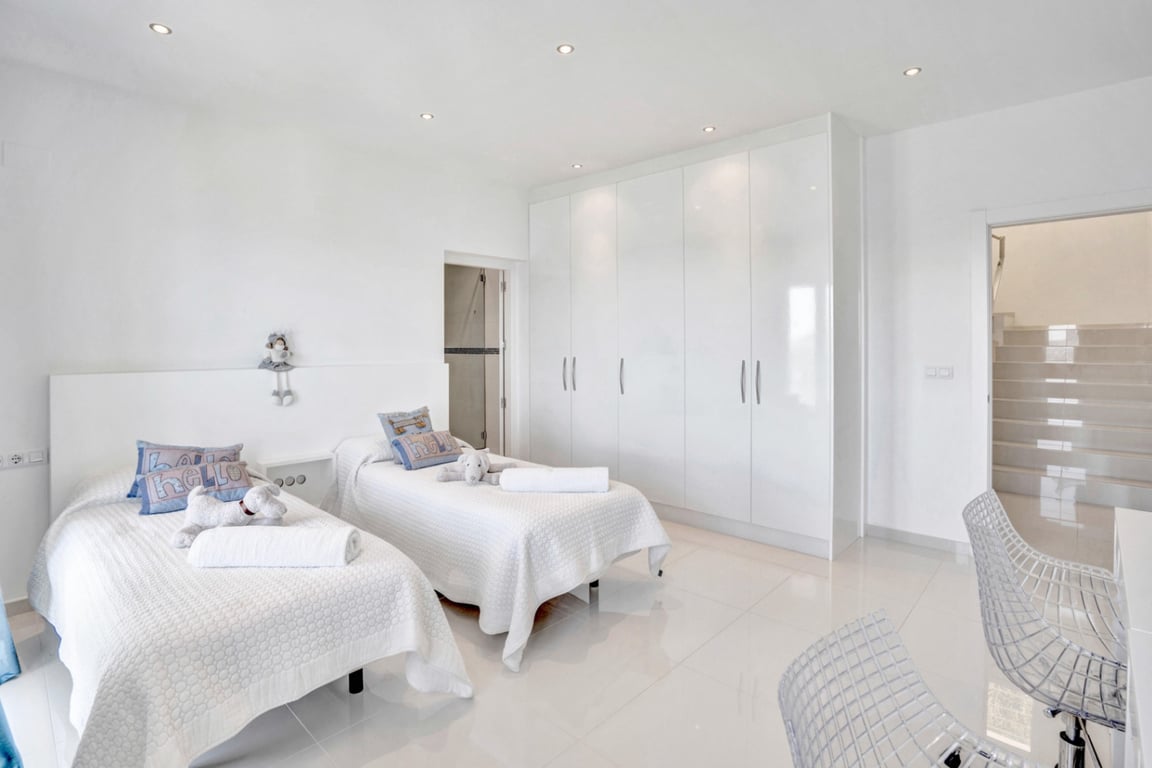 Chambre double minimaliste avec de grands placards intégrés laqués, un sol en grès cérame poli et un éclairage par spots encastrés.