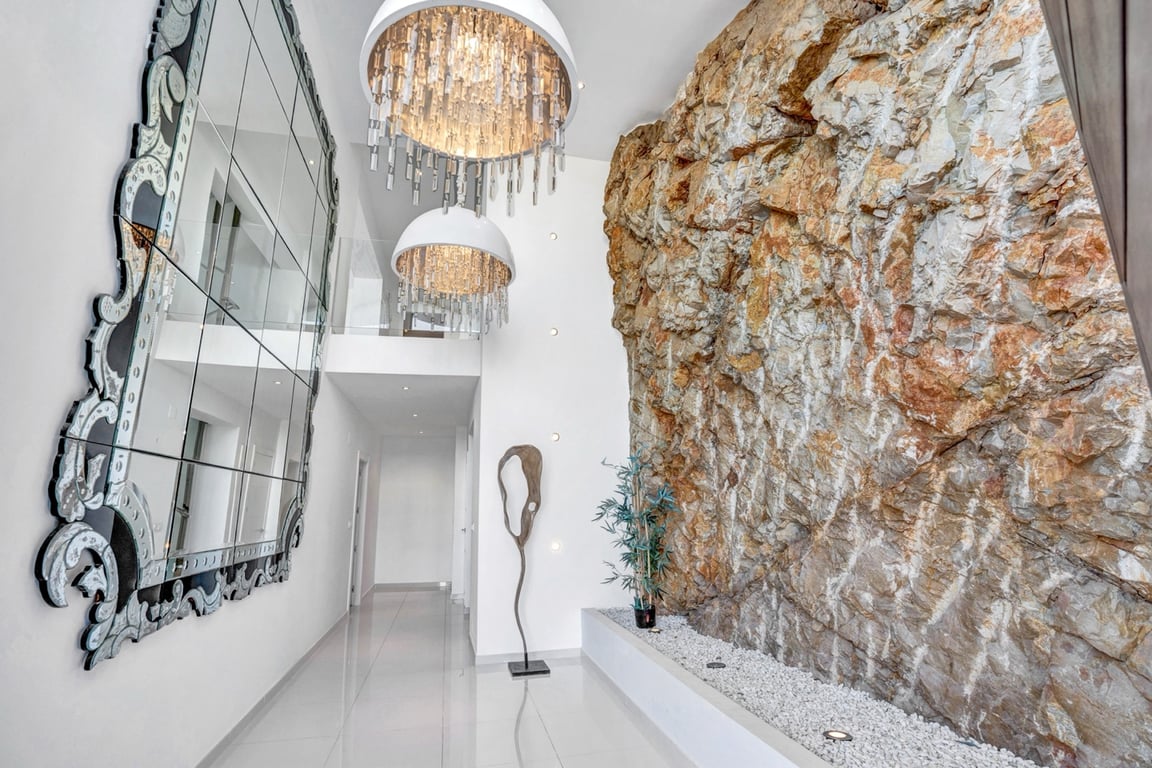 Couloir à double hauteur avec paroi en roche naturelle intégrée, lustres en cristal design et grand miroir orné sur sol en grès poli.