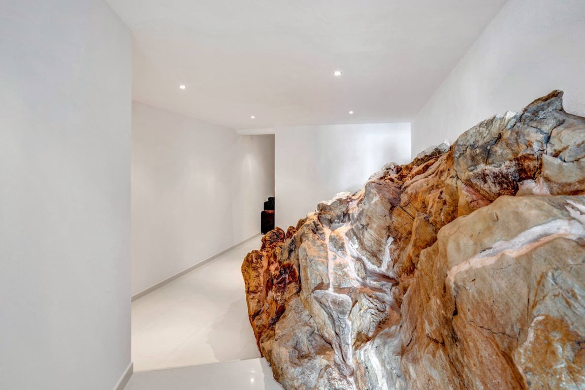 Couloir intérieur avec formation rocheuse naturelle intégrée à l'architecture, murs blancs minimalistes et éclairage encastré au plafond.