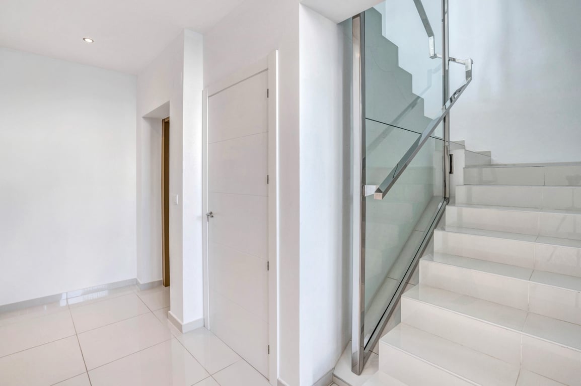 Couloir intérieur moderne avec carrelage blanc et escalier design doté d'un garde-corps en verre et acier inoxydable.