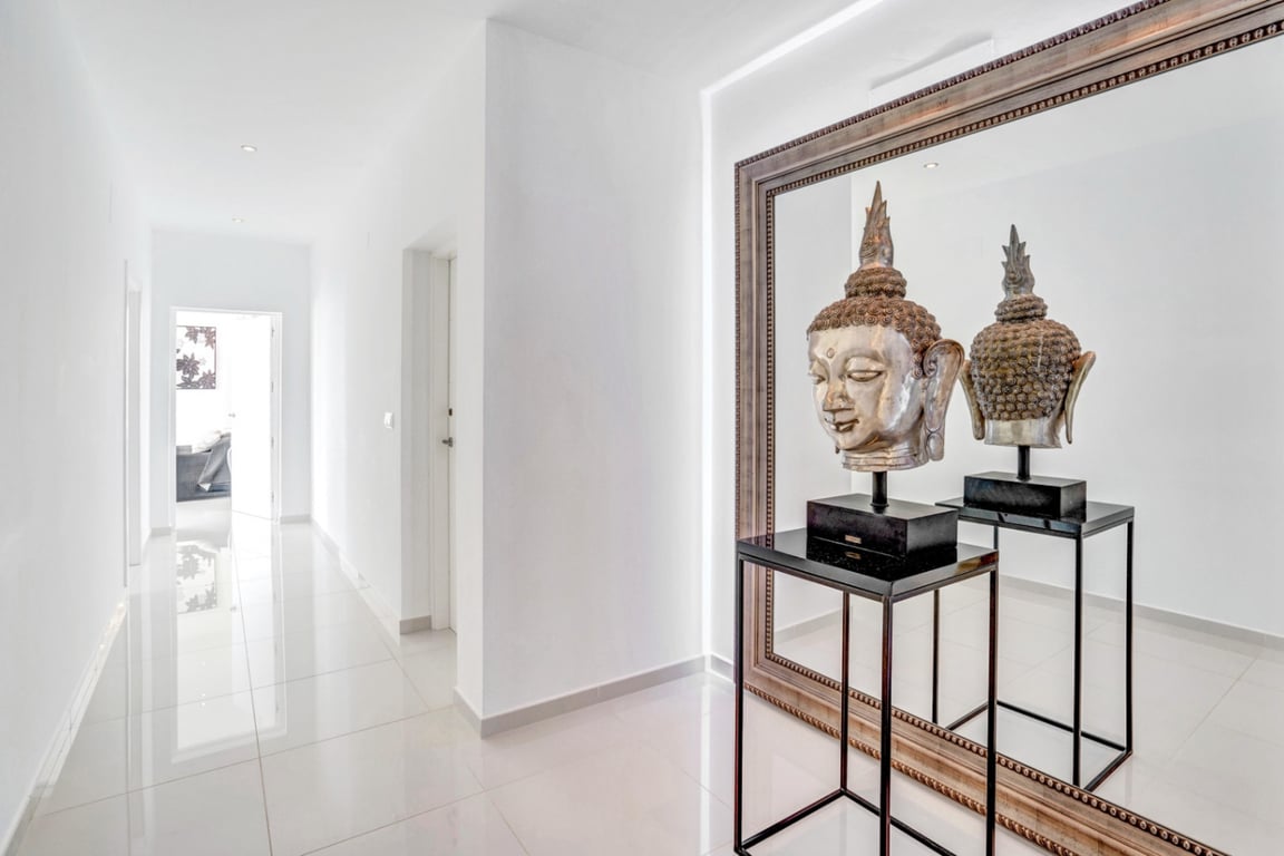 Couloir minimaliste avec sol en grès poli et éclairage encastré. Un grand miroir encadré reflète une sculpture de tête de Bouddha argentée sur un socle noir.