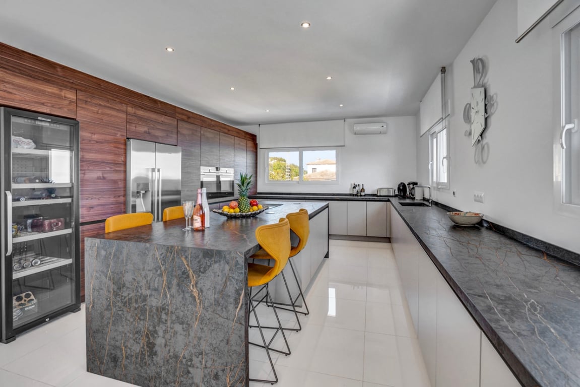 Cuisine moderne avec îlot central en pierre sombre, tabourets jaunes, cave à vin intégrée et finitions en bois naturel élégantes.