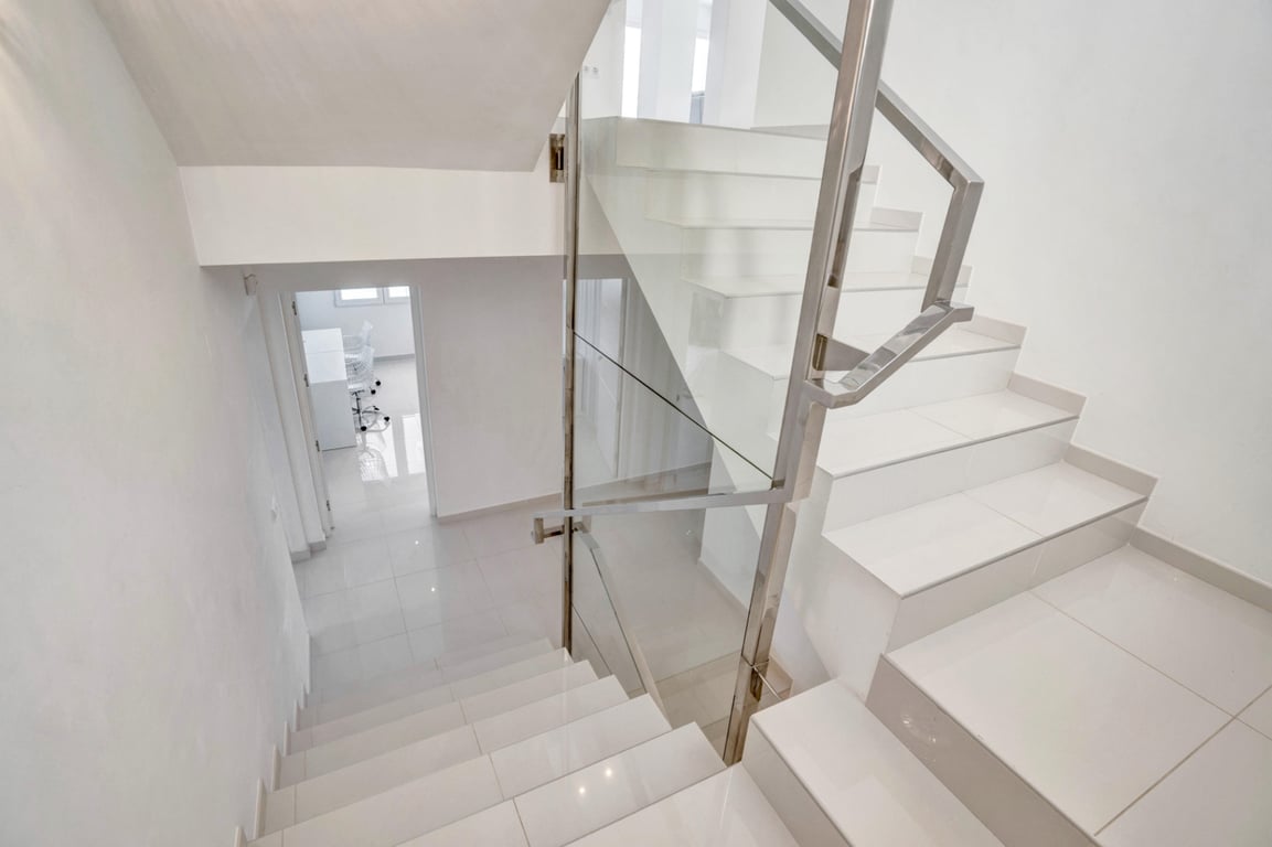 Escalier moderne aux marches blanches, garde-corps en verre et acier inoxydable, offrant un design épuré et une luminosité optimale.