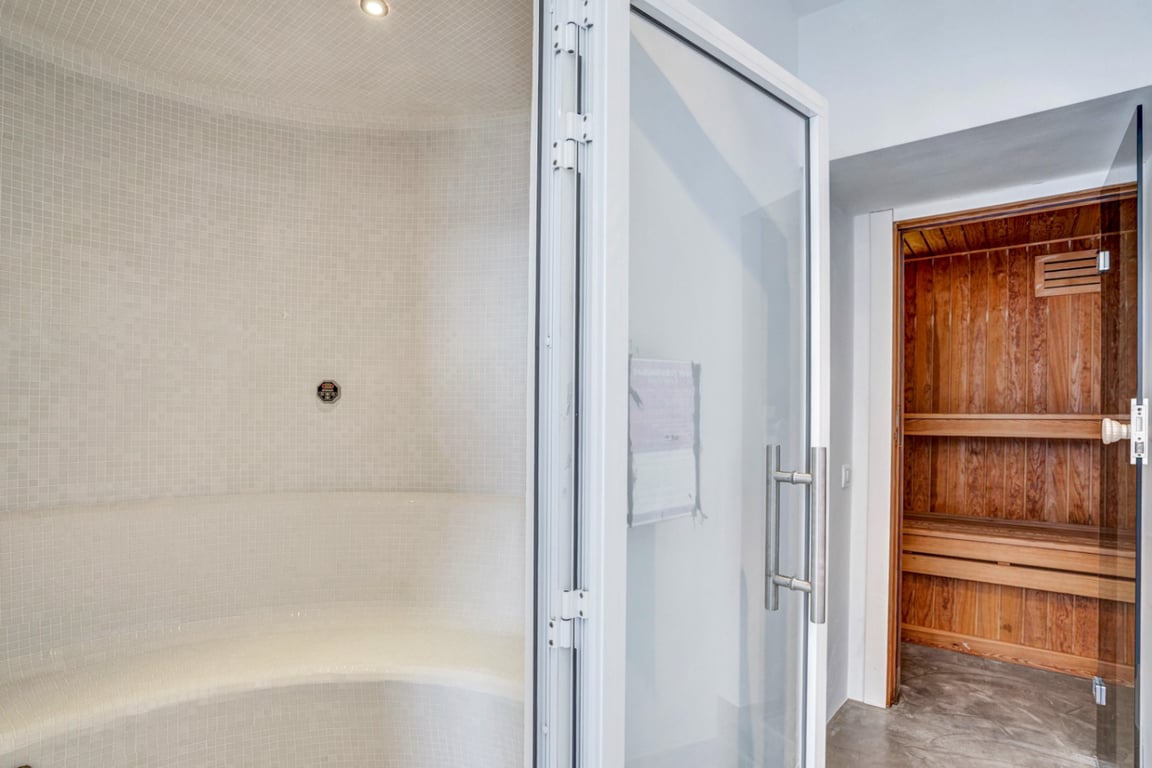 Espace bien-être comprenant un hammam en mosaïque blanche et un sauna finlandais en bois naturel, conçus pour la détente privée.