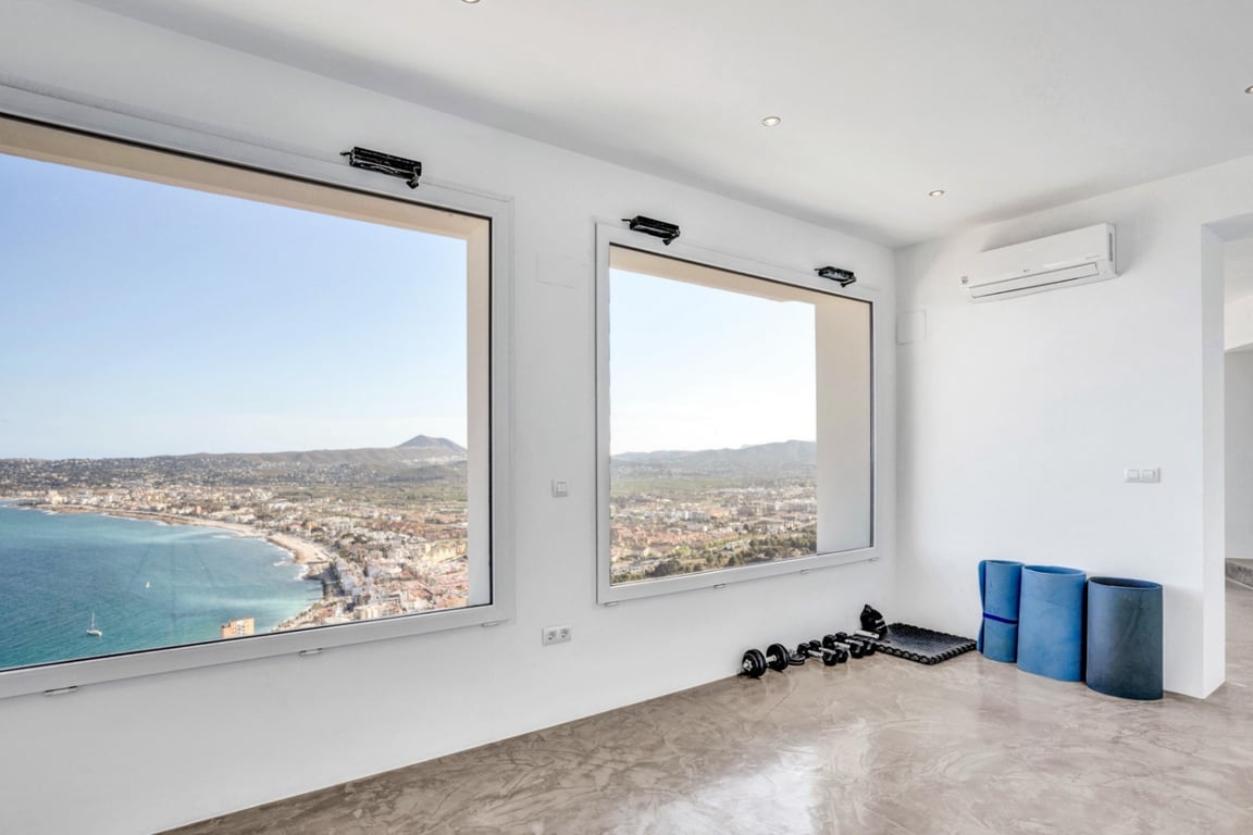 Espace de yoga et fitness avec sol en microciment poli et larges baies vitrées offrant une vue panoramique sur la baie de Jávea et la mer.