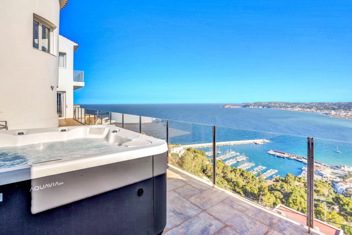 Jacuzzi extérieur Aquavia Spa sur une terrasse en pierre avec garde-corps en verre, offrant une vue panoramique sur le port de Jávea et la Méditerranée.