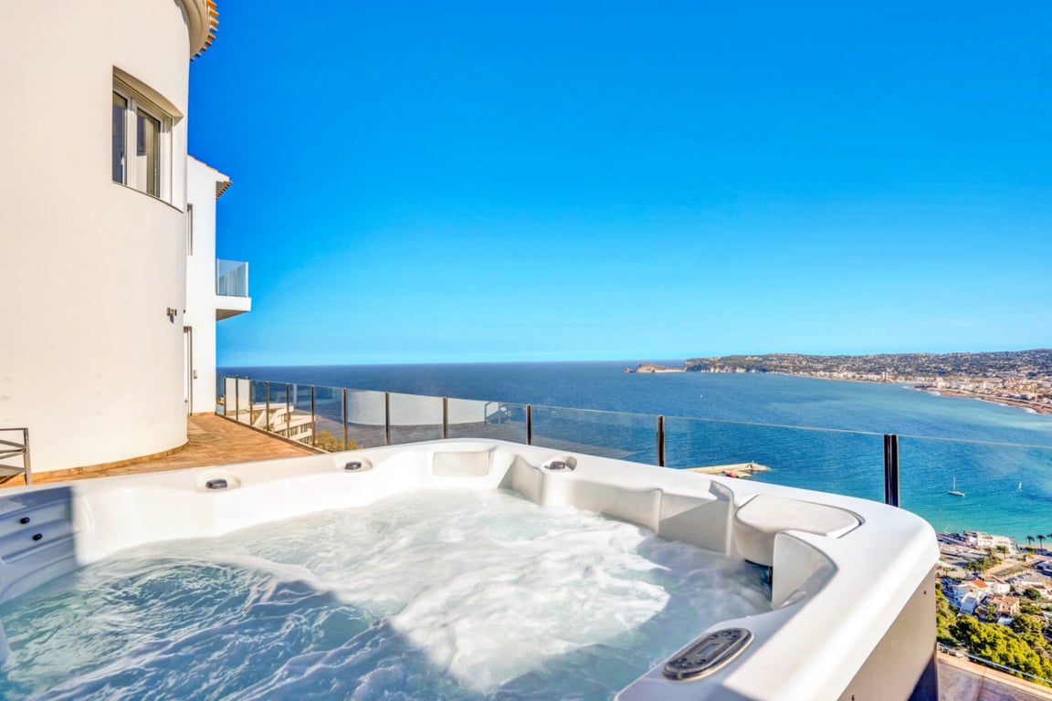 Jacuzzi extérieur sur une terrasse avec garde-corps en verre, offrant une vue panoramique sur la mer Méditerranée et le port de Jávea.