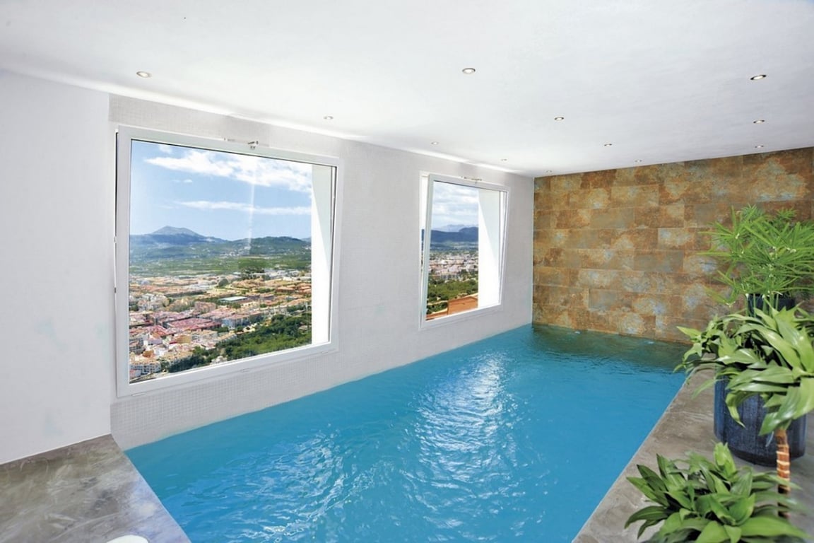 Piscine intérieure chauffée avec de larges fenêtres offrant une vue panoramique sur la vallée, agrémentée d'un mur en pierre naturelle et d'un éclairage encastré.