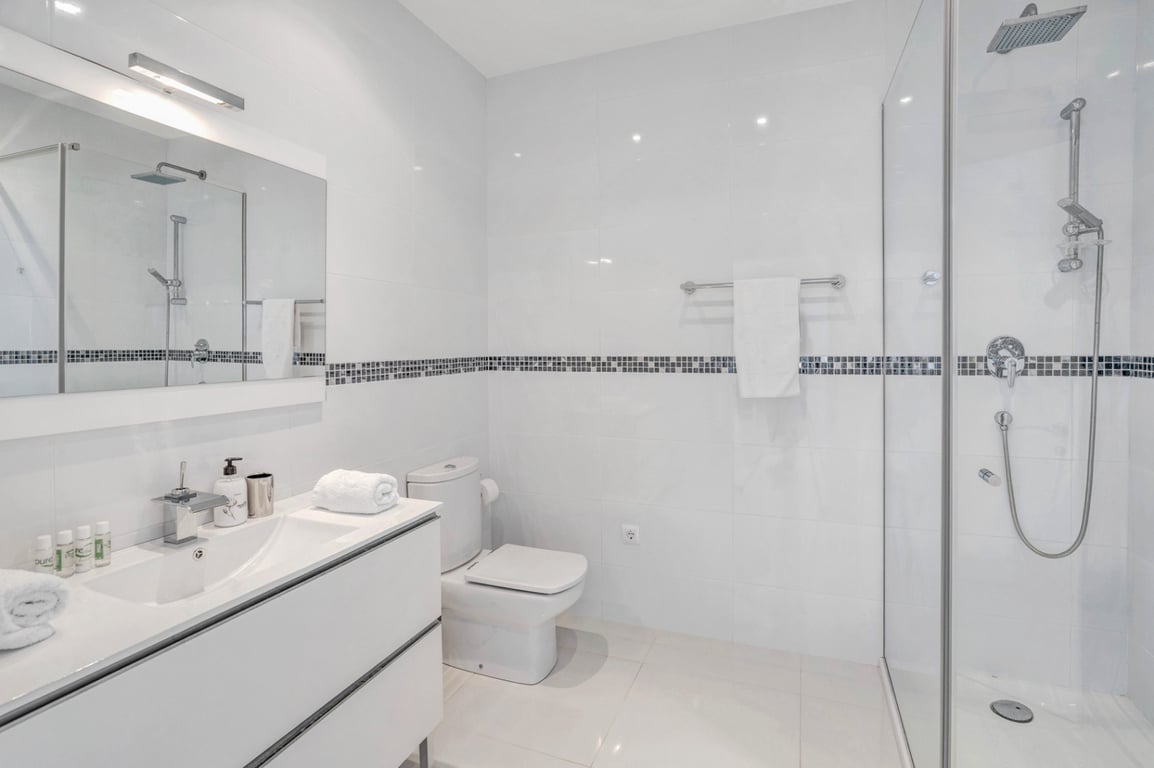 Salle de bain moderne avec carrelage blanc et frise en mosaïque, meuble vasque blanc et douche à l'italienne avec paroi vitrée et robinetterie chromée.