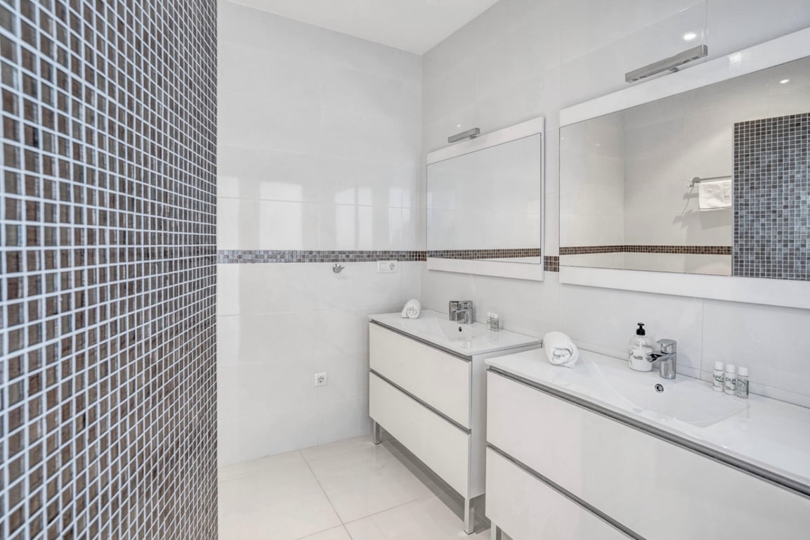 Salle de bain moderne avec double vasque indépendante, meubles blancs épurés et miroirs encadrés soulignés par une frise en mosaïque.
