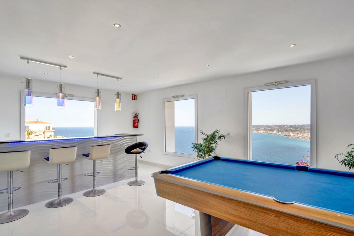 Salle de jeux avec billard bleu et bar moderne éclairé par LED, offrant une vue panoramique sur la mer Méditerranée à travers de grandes fenêtres.