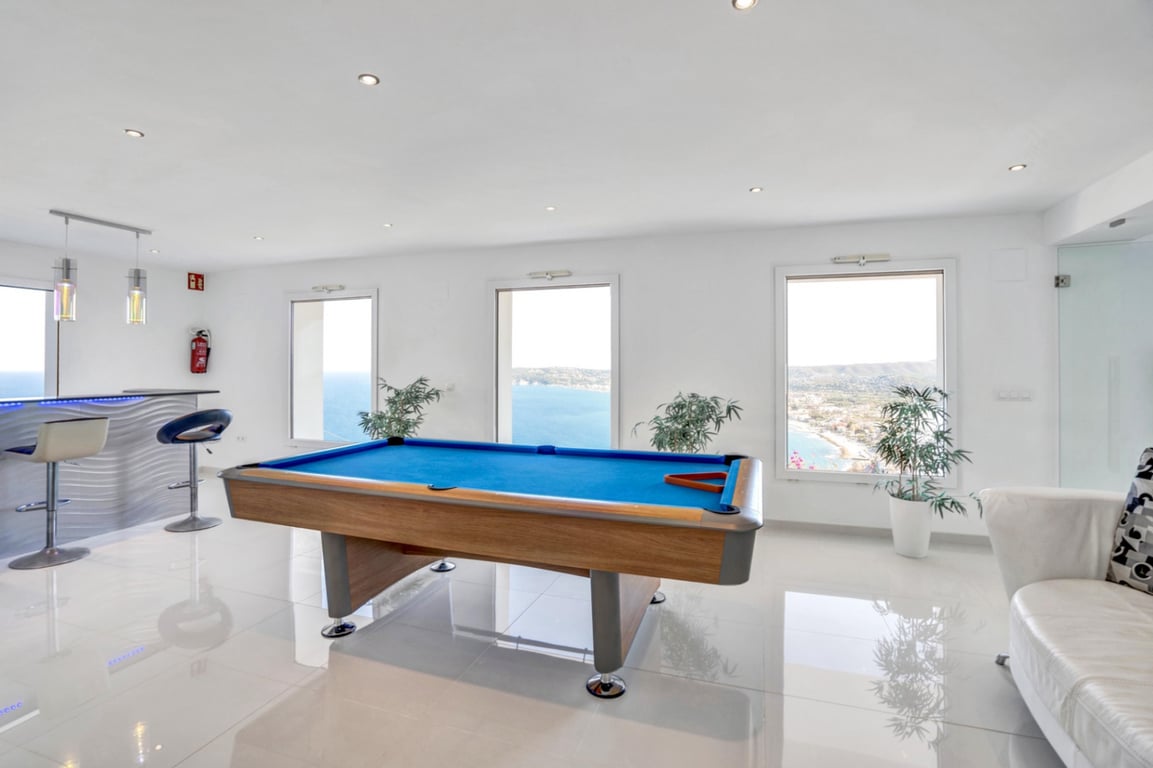 Salle de jeux avec billard, espace bar et grandes fenêtres offrant une vue panoramique sur la mer Méditerranée et la côte de Jávea.