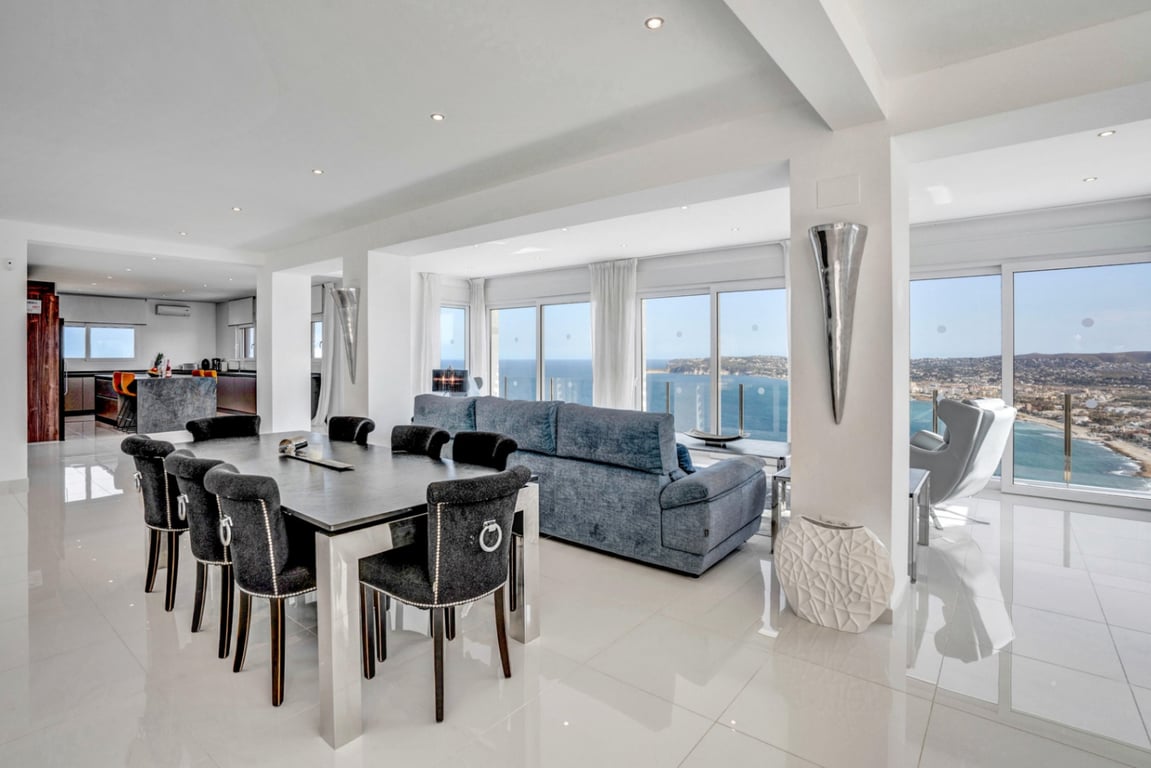 Salon et salle à manger à aire ouverte avec sols polis, mobilier moderne et grandes baies vitrées offrant une vue panoramique sur la mer et la baie.