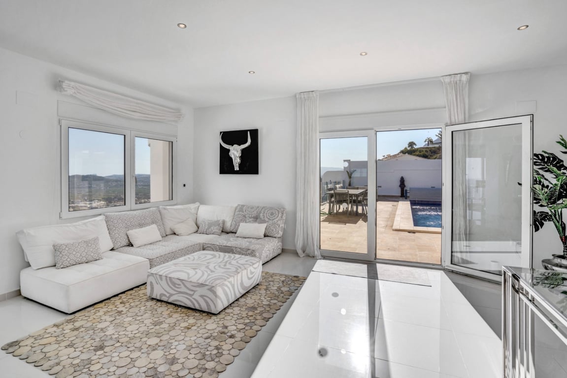 Salon lumineux avec canapé modulaire et accès direct à la terrasse avec piscine, offrant une vue dégagée sur la mer et les montagnes.