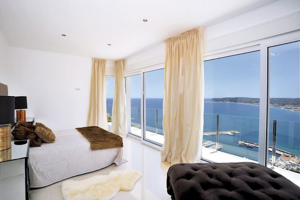 Suite avec baies vitrées offrant une vue panoramique sur le port de Jávea et la mer. Sols polis, éclairage encastré et accès direct à la terrasse avec garde-corps en verre.
