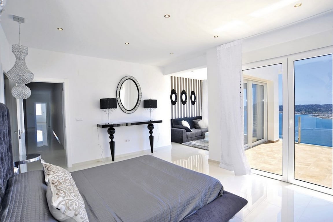 Suite parentale avec sols en grès blanc, coin salon attenant et accès direct à une terrasse offrant une vue panoramique sur la baie de Jávea.