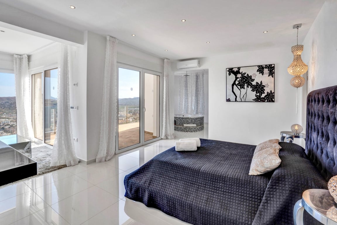 Suite parentale avec tête de lit capitonnée, sol en grès cérame brillant et accès terrasse. Un jacuzzi intégré en mosaïque complète cet espace avec vue mer.