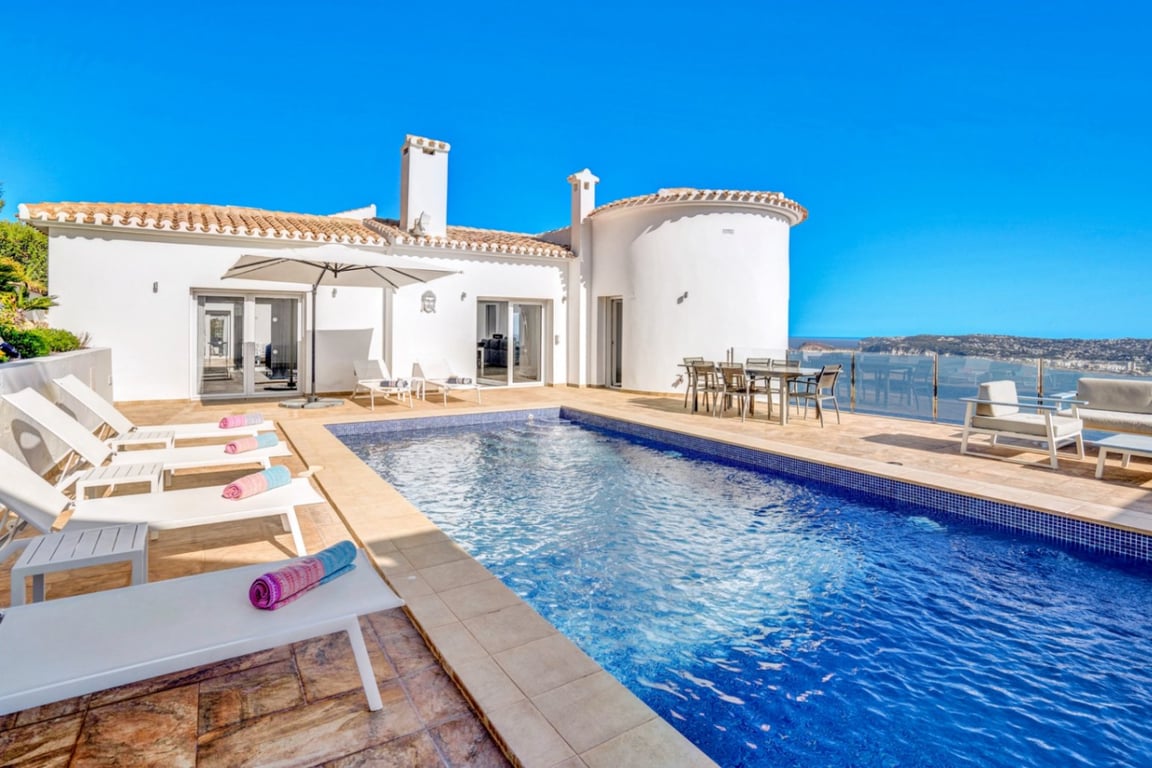 Terrasse principale avec piscine extérieure, espace solarium et coin repas offrant une vue panoramique sur la mer et le port de Jávea.
