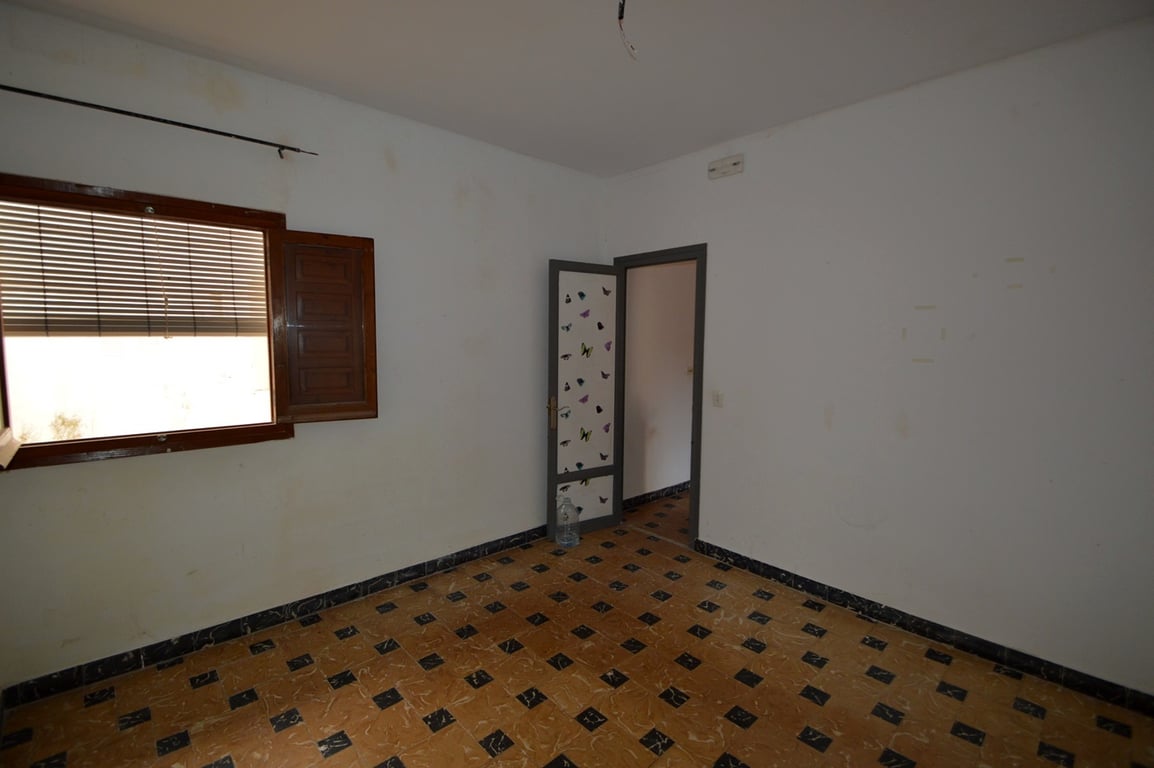 Chambre avec sol en carrelage traditionnel à motifs, murs blancs et fenêtre en bois avec volets. Une pièce à rénover offrant de beaux volumes.