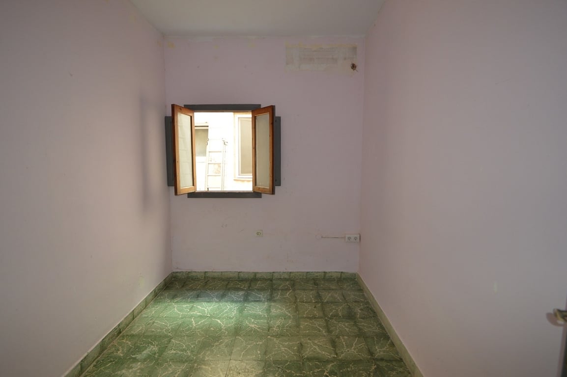 Chambre intérieure avec un sol en carrelage vert marbré, des murs lilas clair et une fenêtre en bois offrant une ventilation naturelle.
