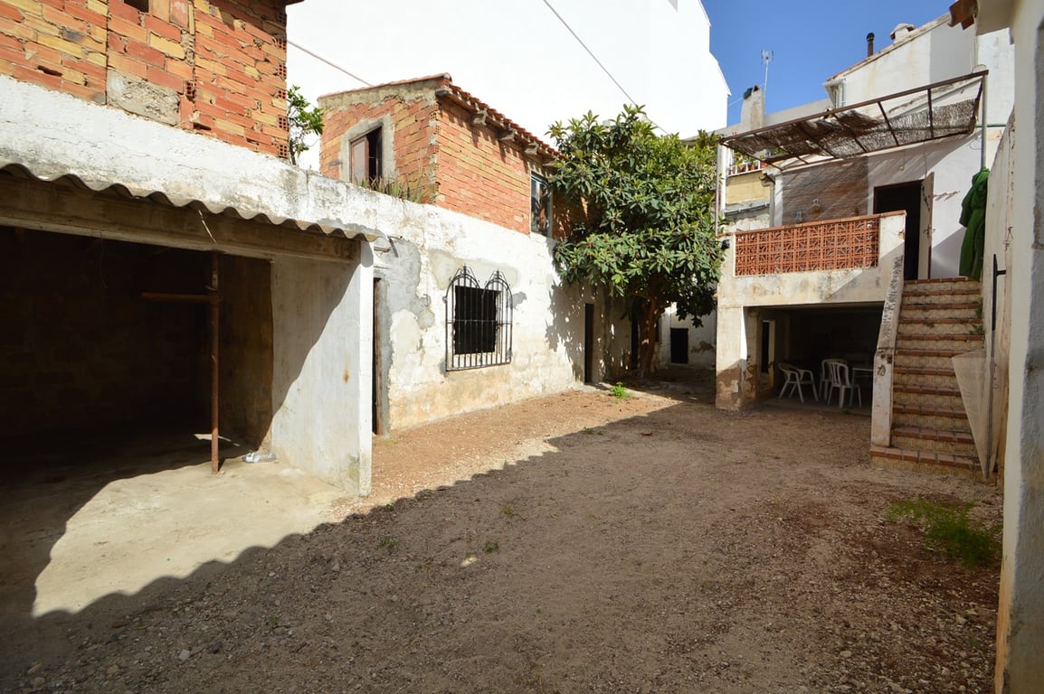 Cour intérieure privée avec sol en terre battue, dépendances en briques apparentes et une terrasse surélevée accessible par un escalier extérieur.