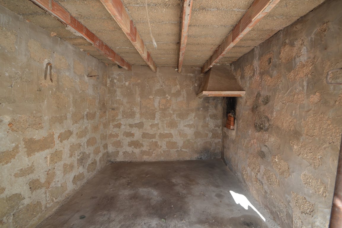 Espace brut avec murs en pierre apparente, poutres en bois au plafond et cheminée d'angle, idéal pour un projet de rénovation en studio ou atelier.