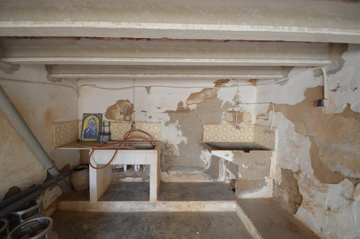 Espace buanderie rustique avec éviers d'origine en pierre, carrelage décoratif et poutres apparentes, prêt pour une rénovation complète.