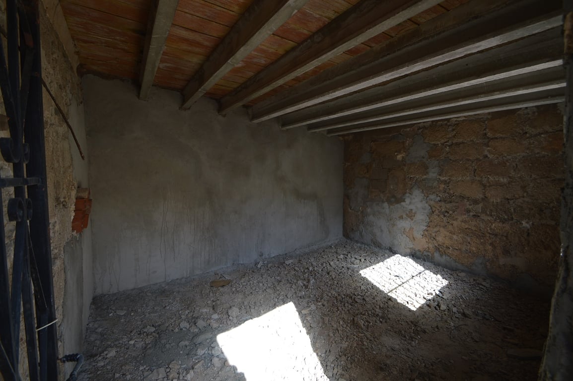 Espace de rangement brut avec murs en pierre d'origine, poutres apparentes et sol en terre, offrant un grand potentiel de transformation en atelier.