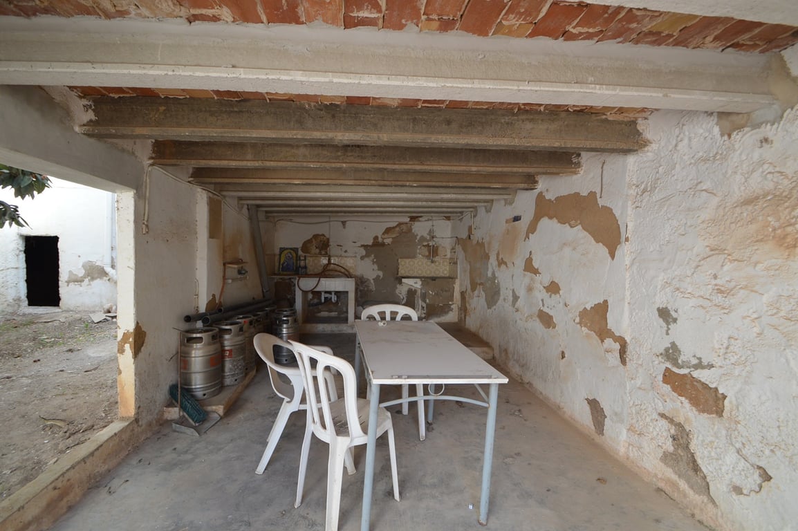 Espace terrasse couvert avec plafonds en briques et poutres en béton, offrant un grand potentiel de rénovation pour un coin repas extérieur.